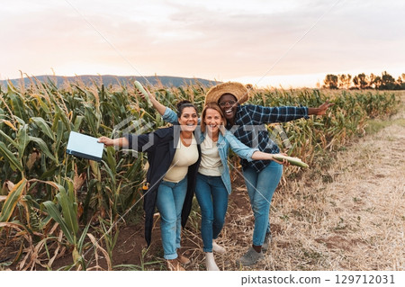 Happy farmers women showing corn harvest in field at sunset 129712031