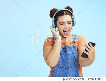Mockup, smartphone and woman with headphones, excited and smile on blue studio background. Happy, female or girl with cellphone, headset or steaming music, social media or podcast to relax or listen 129712045