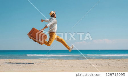A joyful man in a hat and sunglasses leaps enthusiastically on a sandy beach, holding a vintage suitcase, with the blue sea and sky in background. Captures the essence of vacation, freedom, happiness 129712095