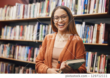 Face, student and woman in university in library ready for learning. Portrait, education and happy female from Brazil standing by bookshelf with book for studying, knowledge and literature research. 129712111