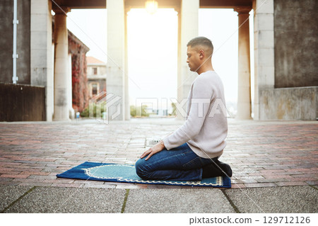 Muslim, faith and praying with an islamic man prayer to god on a carpet for eid or ramadan while fasting. Worship, holy devotion and islam with an arab male kneeling to pray for peace or trust 129712126