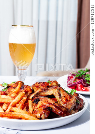Delicious barbecue chicken wings, with French fries, salad and a refreshing drink, at a cozy table, there are no people Delicious barbecue chicken wings, with French fries, salad and a refreshing drink, at a cozy table, there are no people 129712512