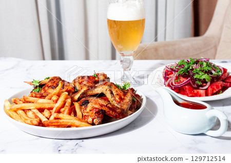 Delicious barbecue chicken wings, with French fries, salad and a refreshing drink, at a cozy table, there are no people Delicious barbecue chicken wings, with French fries, salad and a refreshing drink, at a cozy table, there are no people 129712514