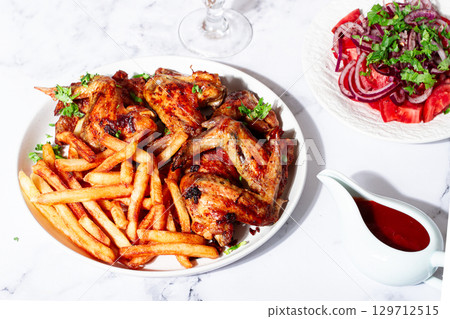 Delicious barbecue chicken wings, with French fries, salad and a refreshing drink, at a cozy table, there are no people Delicious barbecue chicken wings, with French fries, salad and a refreshing drink, at a cozy table, there are no people 129712515