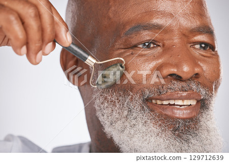Senior man, skin massage and facial roller for skincare, self care and dermatology with a beauty tool. Headshot of black male with a rose quartz on grey studio background for anti aging spa treatment 129712639