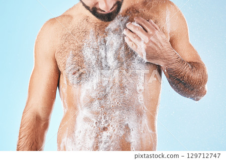 Shower, water and man with soap on body for cleaning, washing and hygiene on blue background studio. Grooming, bathroom and torso of male with foam sponge for skincare, spa wellness and body care 129712747