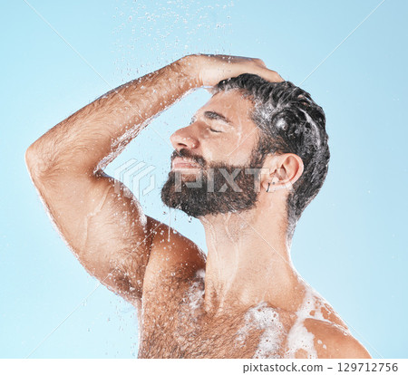Face, water splash and shampoo shower of man in studio isolated on a blue background. Water drops, hair care hygiene and male model washing, cleaning or bathing for healthy skin, wellness or skincare Face, water splash and shampoo shower of man in studio isolated on a blue background. Water drops, hair care hygiene and male model washing, cleaning or bathing for healthy skin, wellness or skincare 129712756