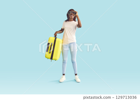 Happy smiling woman holding suitcase and looking through binoculars on blue background. 129713036