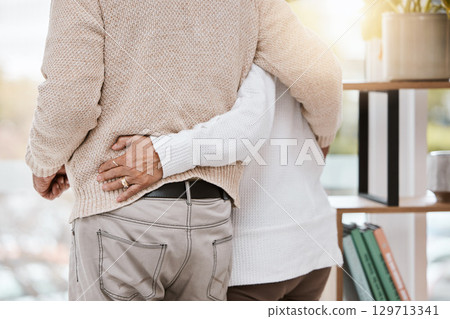 Love, hug and senior couple in their home standing, bonding and spending quality time together. Care, support and elderly woman in retirement holding husband while watching the sunset at their house. 129713341