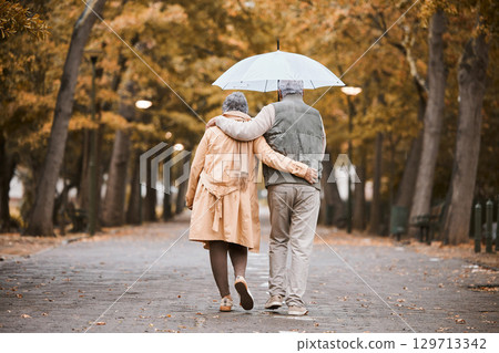 Elderly, couple walk in park with umbrella and fresh air, outdoor in nature in fall for exercise and retirement together. Hug, love and care with trees, senior man and woman in New York back view. 129713342
