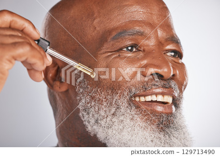 Skincare, wellness and man with a face serum in a studio for a healthy, cosmetic and natural routine. Beauty, cosmetics and African male with a facial oil treatment isolated by a gray background. 129713490