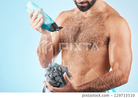 Shower gel, body care and man in a studio for skin hygiene, health and wellness after a shower. Soap, morning routine and male model cleaning or washing his wet body with a sponge by blue background. 129713510