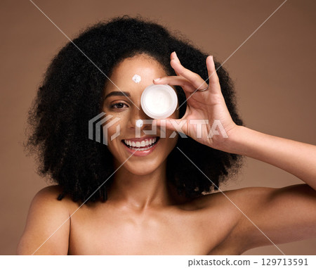 Portrait, container and beauty with a model black woman in studio on a brown background for skin treatment. Face, product and skincare with an attractive young female posing to promote antiaging care Portrait, container and beauty with a model black woman in studio on a brown background for skin treatment. Face, product and skincare with an attractive young female posing to promote antiaging care 129713591