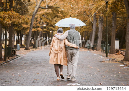 Elderly, couple walk in park with umbrella and fresh air, outdoor in nature in fall for exercise and retirement together. Hug, love and care with trees, senior man and woman in New York back view. 129713634