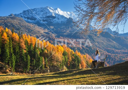 Woman sitting on a bench in autumn forest in the Swiss Alps 129713919