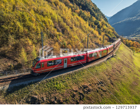 Aerial view of red train in alpine mountains with green meadows 129713937