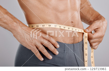 Man, body and tape measure on waist in studio on gray background. Health, fitness and male model with measuring tape for abdomen to track exercise training results, muscle goals or weight loss target 129713961