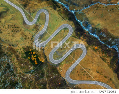 Aerial view of winding mountain road, river in alpine valley 129713963