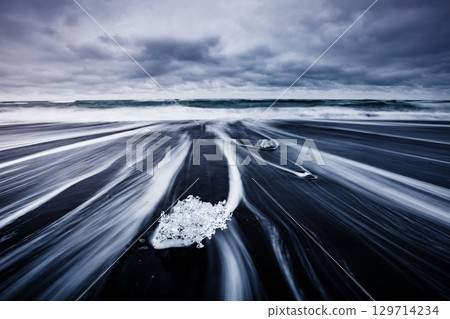 Pieces of the iceberg sparkle on the black sand. 129714234