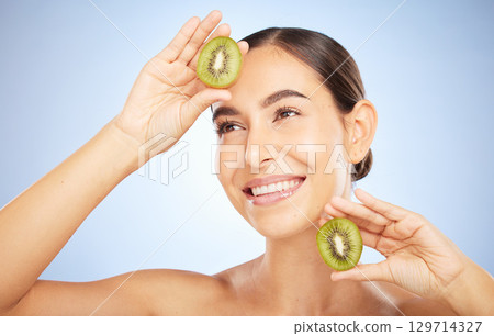 Beauty, kiwi and woman with face and smile, skincare and organic, vegan cosmetic care for healthy skin. Microblading, natural cosmetics and hands frame with fruit, facial and glow on blue background. 129714327