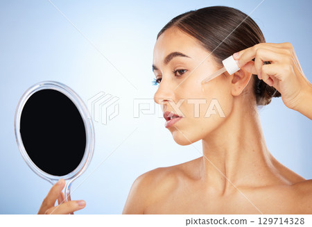 Skincare, hand mirror and woman with serum, natural beauty and cosmetics on blue studio background. Makeup, female and oil for dermatology, luxury and smooth skin for wellness, healthcare and routine 129714328