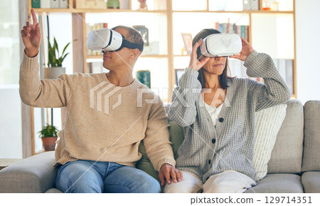 Virtual reality, 3d and a couple in the interactive metaverse while together on a sofa in the living room of a home. VR, goggles and gaming with a man and woman in their house to relax or video game Virtual reality, 3d and a couple in the interactive metaverse while together on a sofa in the living room of a home. VR, goggles and gaming with a man and woman in their house to relax or video game 129714351