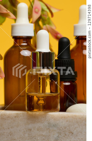 Glass dropper bottle with a silver cap and a white dropper dripping amber liquid Glass dropper bottle with a silver cap and a white dropper dripping amber liquid 129714398