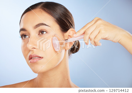 Woman, face or rose quartz roller for skincare grooming on blue background gradient for collagen treatment, wrinkles or lymph fluid wellness. Zoom, glowing or beauty model with facial stone massage 129714412