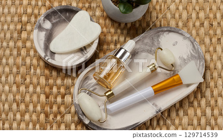 Facial care items lying on an oval tray. A bottle with a pipette and two facial massage rollers 129714539