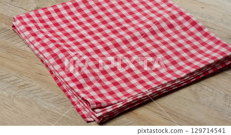 A folded red and white checkered textile towel lying on a wooden surface. 129714541