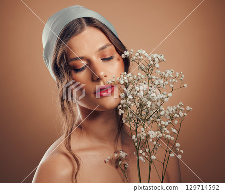 Woman, face or skincare glow with flowers on brown studio background for organic dermatology, healthcare wellness or vegan facial treatment. Beauty model, scarf or plant bouquet with makeup cosmetics 129714592