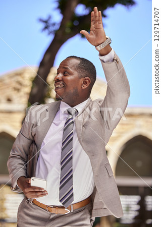 Business, phone or black man wave, hello and travel with connectivity, social media and taxi. Jamaican male, entrepreneur and smartphone with hand gesture for greeting, transport and commute in city. Business, phone or black man wave, hello and travel with connectivity, social media and taxi. Jamaican male, entrepreneur and smartphone with hand gesture for greeting, transport and commute in city. 129714707