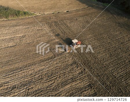 Farmer plowing field with tractor and harrow, aerial view of soil preparation in agriculture. Farmer plowing field with tractor and harrow, aerial view of soil preparation in agriculture. 129714726