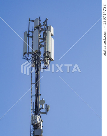 Cellular base station tower with antennas and microwave dishes providing wireless communication services against a clear blue sky ensures seamless connectivity 129714758