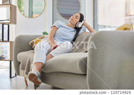 Woman, relax and music headphones on sofa in house, home or hotel living room for mental health, self care or stress management. Zen, student and person listening to radio, podcast or wellness audio 129714929