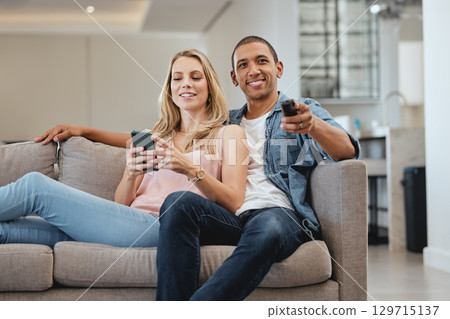 Love, interracial and couple on sofa, relax or watching tv for quality time, weekend or break. Romantic, man with remote for soccer or woman with smartphone for social media, connection and streaming Love, interracial and couple on sofa, relax or watching tv for quality time, weekend or break. Romantic, man with remote for soccer or woman with smartphone for social media, connection and streaming 129715137