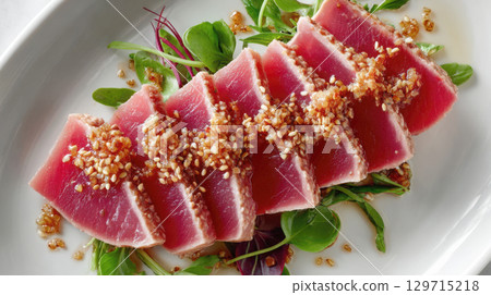 A beautifully plated dish of seared ahi tuna, expertly sliced to reveal its ruby red interior and topped with a sprinkle of toasted sesame seeds, served on a bed of fresh greens 129715218