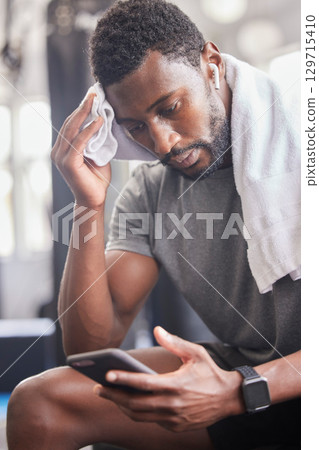 Gym, workout and tired black man with phone for social media and towel for sweat from cardio. Fitness, rest and exercise fatigue of sweaty guy on smartphone app for body relaxation to recover. Gym, workout and tired black man with phone for social media and towel for sweat from cardio. Fitness, rest and exercise fatigue of sweaty guy on smartphone app for body relaxation to recover. 129715410