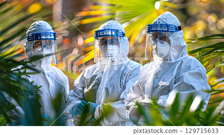 Healthcare professionals in protective gear standing among lush greenery in a vibrant outdoor setting 129715633