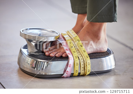 Diet, weight loss and feet of a woman on a scale for body check, measure and balance to lose weight on the floor. Obesity, scales and girl with tape measure for obsession with health and body image Diet, weight loss and feet of a woman on a scale for body check, measure and balance to lose weight on the floor. Obesity, scales and girl with tape measure for obsession with health and body image 129715711