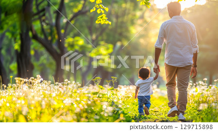 Father and child walking hand in hand through a sunlit park filled with blooming flowers 129715898