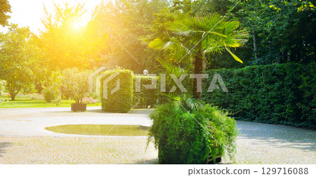 Landscaped park with a garden bed and different trees and bushes on a turf lawn, evergreen and seasonal plants. Landscaped park with a garden bed and different trees and bushes on a turf lawn, evergreen and seasonal plants. 129716088
