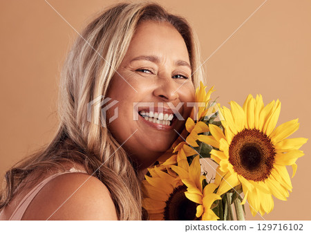 Mature woman and beauty portrait with flower bouquet and happy smile for natural skincare campaign. Wellness, cosmetics and healthy skin of latino person with sunflowers on beige studio background. 129716102