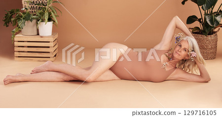 Beauty, body positivity and natural with a senior woman lying on the floor of a studio on a beige background. Portrait, skin and underwear with a mature model female posing for luxury or wellness Beauty, body positivity and natural with a senior woman lying on the floor of a studio on a beige background. Portrait, skin and underwear with a mature model female posing for luxury or wellness 129716105