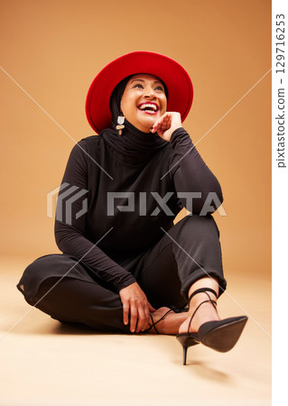 Fashion, beauty and muslim woman in hat in studio on a brown background. Vintage aesthetic, mature or Islamic female model laughing, sitting on floor and thinking of classy, stylish or retro clothing 129716253
