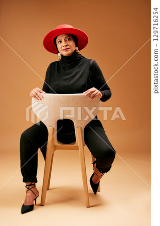 Muslim woman, chair and fashion, beauty and hat with trendy outfit, focus attitude and studio background. Mature Indonesia model, portrait and islamic culture, hijab lifestyle and luxury clothes Muslim woman, chair and fashion, beauty and hat with trendy outfit, focus attitude and studio background. Mature Indonesia model, portrait and islamic culture, hijab lifestyle and luxury clothes 129716254