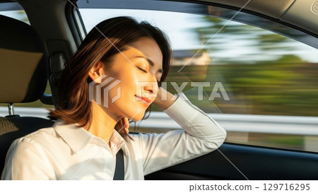 A woman closes her eyes while driving and bathed in light coming through the car window 129716295