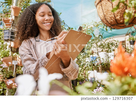 Small business, plants and black woman with inventory, quality control and checklist clipboard in nursery. Smile of satisfied business owner writing quality assurance notes in flower garden. Small business, plants and black woman with inventory, quality control and checklist clipboard in nursery. Smile of satisfied business owner writing quality assurance notes in flower garden. 129716307