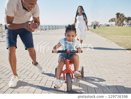 Bike, learning and child with family at beach or city park for growth development, support and motivation of mother and father. Cycling girl on bicycle and african parents travel, summer and teaching 129716396