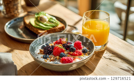 Healthy breakfast with a bowl of fresh berry yogurt, avocado toast and a glass of orange juice in a sun-drenched kitchen Healthy breakfast with a bowl of fresh berry yogurt, avocado toast and a glass of orange juice in a sun-drenched kitchen 129716521